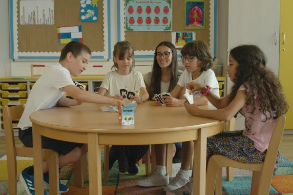 Enfants jouant au jeu de cartes Nutrino autour d'une table, apprenant la nutrition de façon ludique